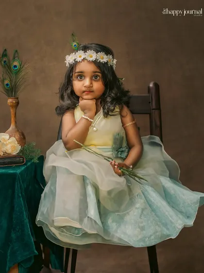 A thoughtful portrait of a girl in a pastel gown and a daisy crown. The peacock feathers in the background add an artistic, traditional touch.