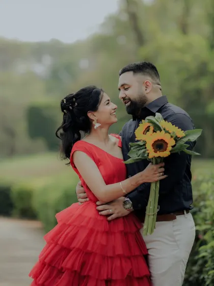 A beautiful pose during a pre-wedding session in a Pune garden. The woman's vibrant red dress stands out against the green foliage, creating a visually stunning and romantic photograph.