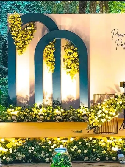 A classy and modern engagement setup for an outdoor event. The deep teal arches with cascading yellow flowers create a stunning contrast against the natural greenery.