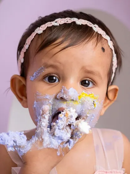 The aftermath of a successful cake smash! This close-up shot is all about the messy, happy reality of turning one. Her beautiful eyes and frosting-covered face make for an unforgettable portrait.