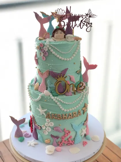 A grand two-tiered mermaid cake, featuring an ocean-green buttercream, pearl details, and shimmering mermaid tails.