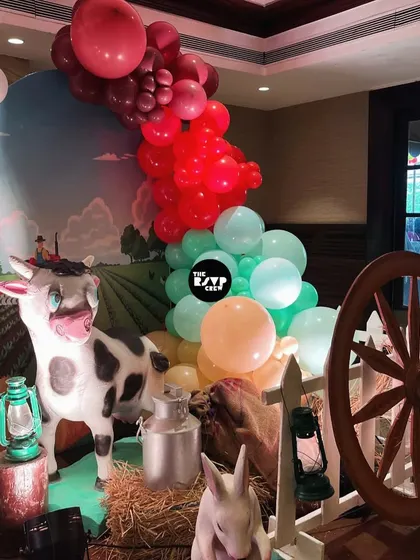 A life-sized cow prop with a milk pail, a wagon wheel, and a colorful balloon garland added to the authentic farm feel.
