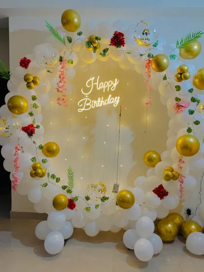 An elegant birthday backdrop with a white and gold balloon ring, decorated with artificial flowers and vines.