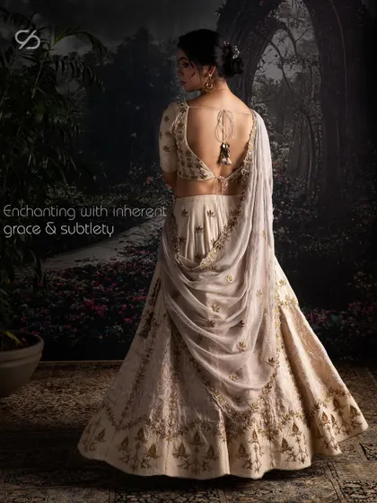 This Moonga Silk lehenga, with its enchanting back detail and gentle brocade touches, offers a vision of understated opulence. The artful drape and exquisite craftsmanship are designed for a bride with a subtle yet commanding presence.