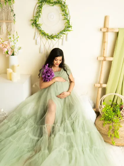 A serene seated portrait in a green gown, holding a bouquet of purple flowers. The contrasting colors create a visually interesting image.