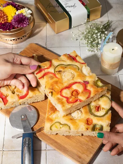 A lifestyle shot of hands sharing a slice of savory vegetable focaccia bread, creating a warm, communal feel.