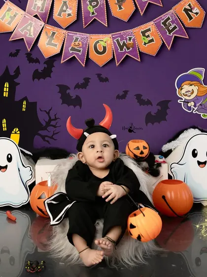 A little devilishly cute baby posing for our Halloween mini session. The setup includes friendly ghosts, pumpkins, and a festive banner.