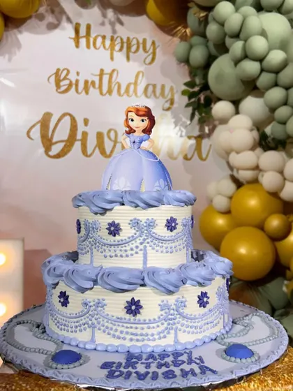 A royal celebration for a little princess. This two-tier cake features a Princess Sofia topper and elegant purple piping details, fit for a birthday girl named Divisha.
