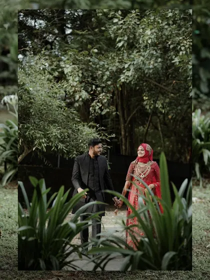 Framed by greenery, this shot captures the couple in a quiet moment during their walk, highlighting the bride's beautiful red attire.