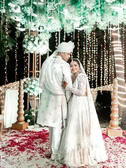A classic wedding portrait with the groom holding his bride close, showcasing the beautiful details of their all-white wedding attire.