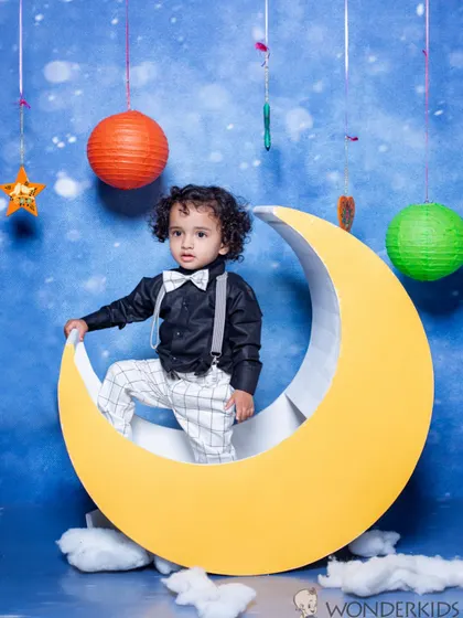 A dapper little boy in a black shirt and bow tie, posing confidently on a crescent moon prop. This stylish and imaginative setup is great for capturing a toddler's personality.