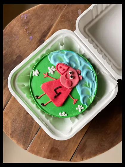A fun and colorful Peppa Pig bento cake for a 4th birthday. Peppa is shown lying in the grass next to a puddle, just like in the show.