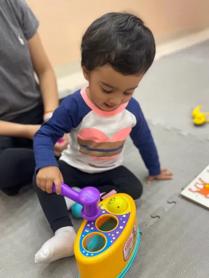 A toddler uses a toy hammer, an activity that improves hand-eye coordination and allows for safe, satisfying sensory feedback.