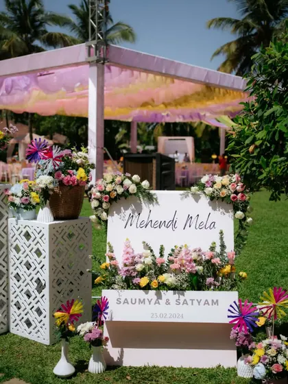 A charming welcome sign for the 'Mehendi Mela,' surrounded by fresh flowers and colorful pinwheels.