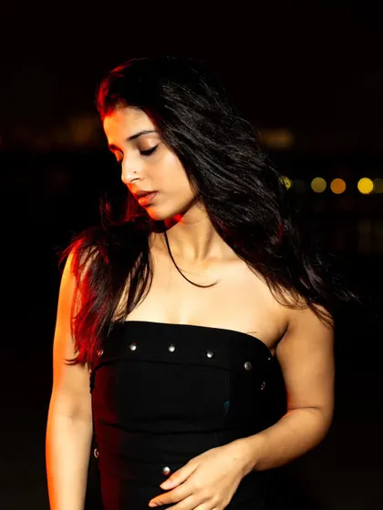 A soft, downward glance lit by flash. This pose creates a quiet, contemplative mood amidst the darkness.