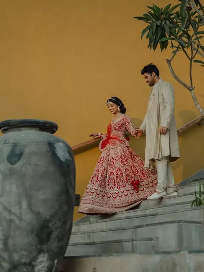 A regal portrait of the couple in their stunning red and cream wedding attire. We use architectural elements like staircases to add a touch of grandeur to our compositions.