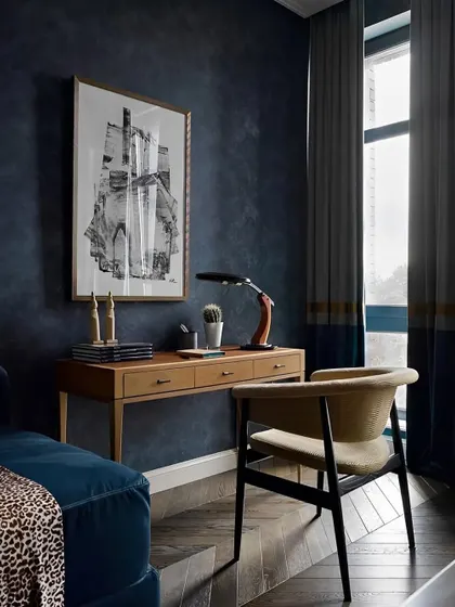 A moody and sophisticated home office with dark blue walls, a wooden desk, and curated art pieces.
