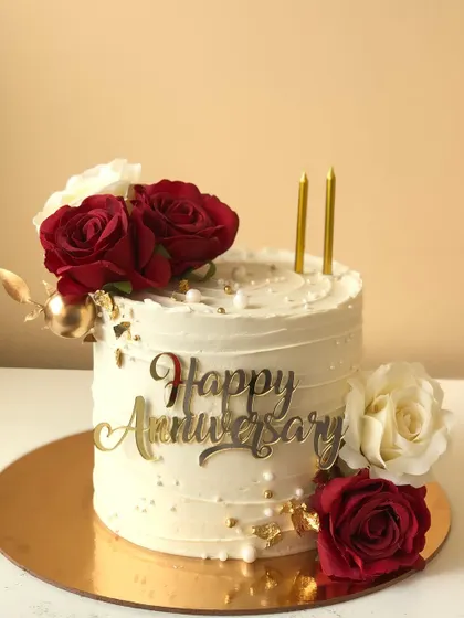 A classic anniversary cake with red and white roses, gold leaf, and a script topper.