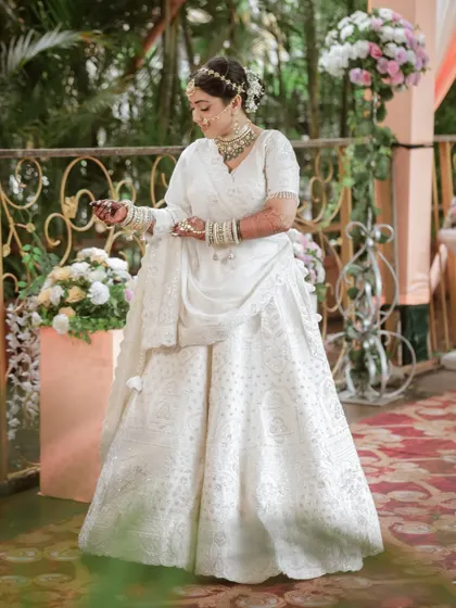 A candid moment of the bride adjusting her bangles, looking graceful and elegant in her all-white wedding lehenga.