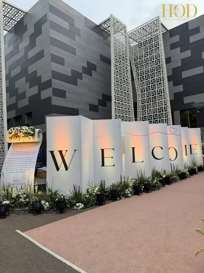 A bold and simple "WELCOME" sign, elegantly designed with large letters and flanked by white flowers. This creates a clean, modern, and impactful statement at the entrance of the event.