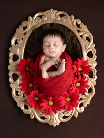 A beautiful portrait within a portrait. This newborn, wrapped in red and framed by flowers, looks like a timeless painting.
