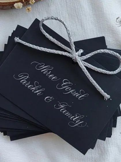 Guest name tags for the 25th-anniversary celebration, handwritten in silver ink on black cardstock to match the elegant black-and-silver theme of the event.