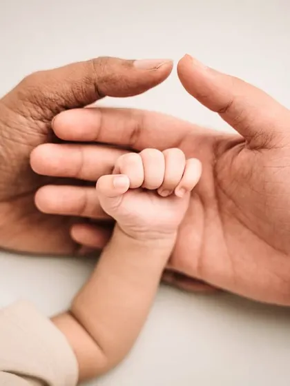A newborn's tiny fist held between the hands of their parents, a symbol of family strength and unity.