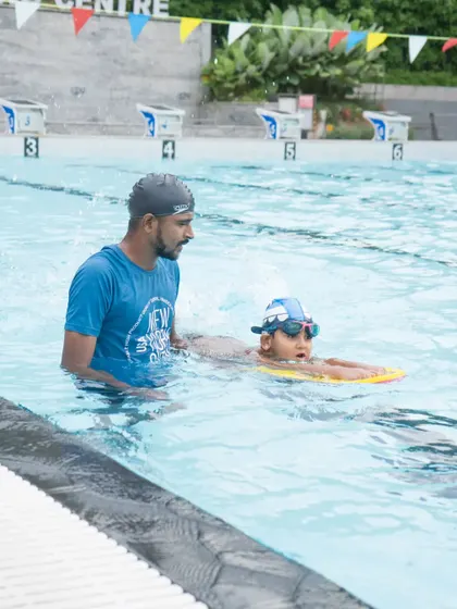 A coach provides in-water support to a young learner, helping them get the feel for moving through the water with a kickboard.