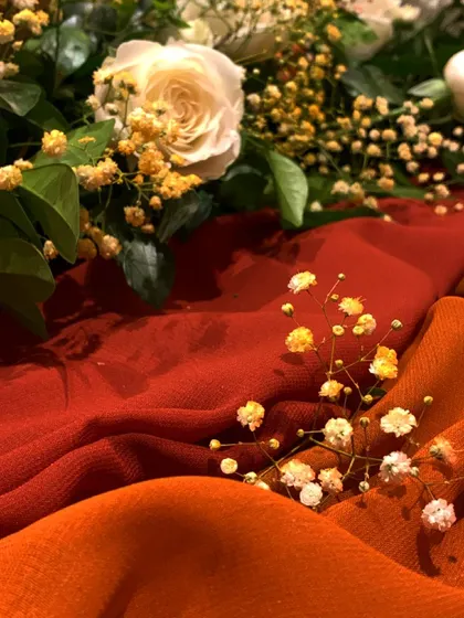 A beautiful detail shot of white roses and yellow baby's breath resting on rich, autumn-colored fabrics. This captures the essence of our warm, seasonal color palette.