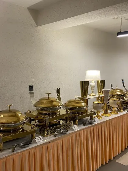 A full view of a main course buffet line for an indoor event. The setup features our signature gold-domed chafing dishes and matching decorative vases on a simple, elegant table skirt.