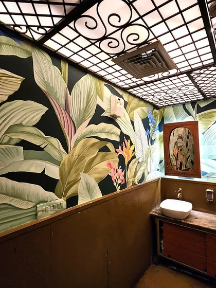 We transformed the washroom at The Drunken Botanist in Gurgaon with this immersive, floor-to-ceiling botanical mural. The dark background makes the lush, green leaves and colorful flowers pop.