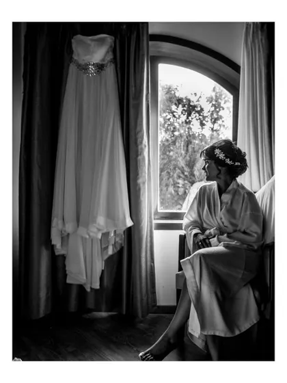 A pensive black and white portrait of a bride in her robe, looking out the window before putting on her wedding dress.