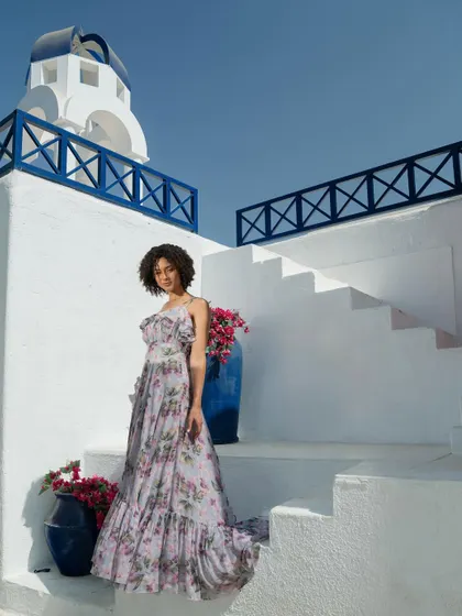 A campaign image for Tangerine Tiger, shot on a Santorini-inspired set. The white and blue architecture provides a beautiful, clean backdrop for the floral maxi dress, creating a destination-wear vibe.