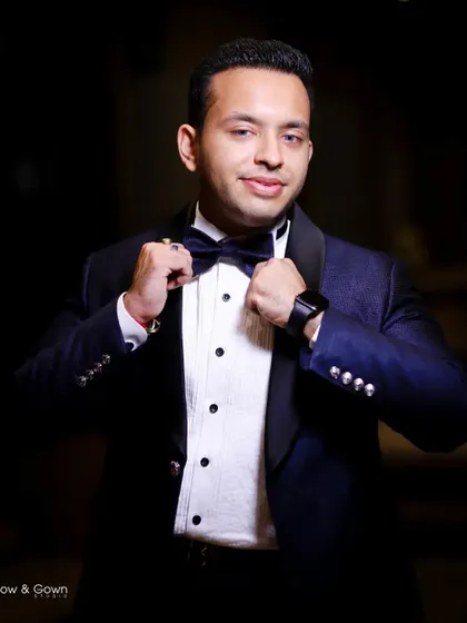 A classic portrait of the groom looking dapper in his tuxedo. He adjusts his bow tie, a confident and stylish shot from his engagement day.