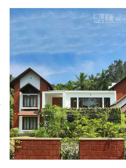 The exterior of Hamdiya House combines traditional sloped roofs with a modern white-walled structure, surrounded by a laterite compound wall and lush greenery.
