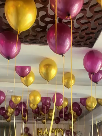 A ceiling full of purple and gold helium balloons with swirling ribbons.