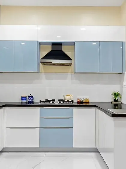 A U-shaped modular kitchen with a clean, modern aesthetic. The combination of light blue and white glossy cabinets makes the space feel bright and airy, while the black countertop adds a sleek contrast.