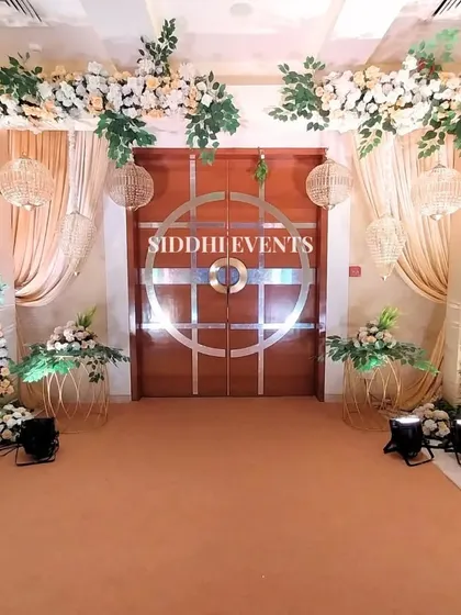 This stunning entrance features a floral archway of lush white blooms and greenery, accented with hanging wicker ball lanterns for a touch of rustic elegance.