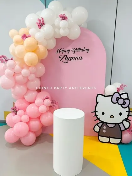 A simple and sweet Hello Kitty theme birthday decoration. The setup features a pink arch backdrop, a character cutout, and a pastel balloon garland.