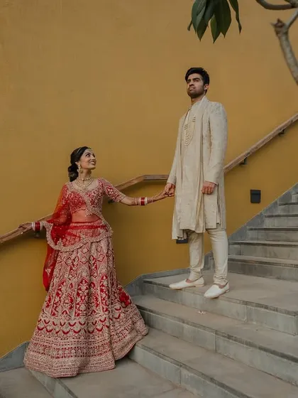 A regal portrait of the couple in their stunning red and cream wedding attire. We use architectural elements like staircases to add a touch of grandeur to our compositions.
