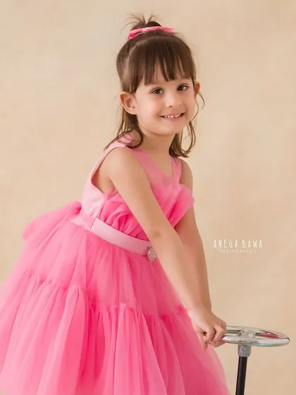 A charming portrait of a little girl in a bright pink dress, holding onto her toy car with a sweet and confident smile.