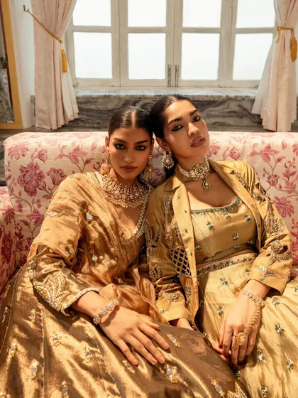 A close-up dual-model shot showcasing the rich, golden tones of the outfits and the models' strong, confident expressions.