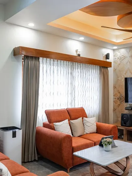 This living room combines warmth and modern style. An orange sofa adds a pop of color, while the marble-patterned accent wall behind the TV and a unique wooden-blade fan create a striking focal point.