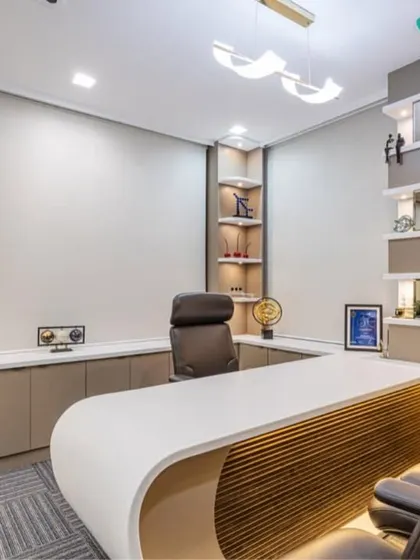 An executive office designed for comfort and style. The space features a curved desk with wood-textured front paneling, built-in display niches with gold accents, and a comfortable seating area, making it ideal for both work and informal client meetings.