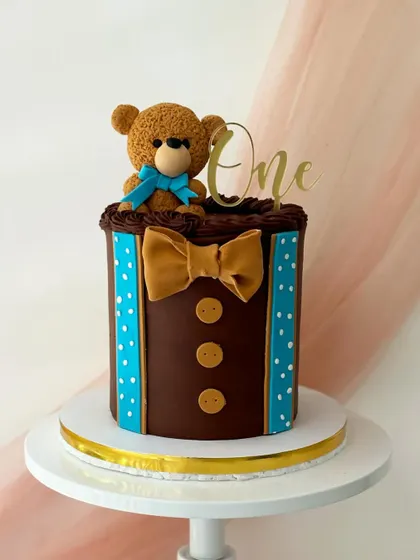 A dapper teddy bear cake for a first birthday. The cake is decorated to look like a little tuxedo, with a chocolate buttercream "vest" and a fondant bow tie.