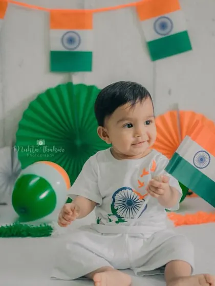 Surrounded by flags and festive decorations, the baby looks on with a happy and engaged expression. A perfect snapshot of a milestone celebration.