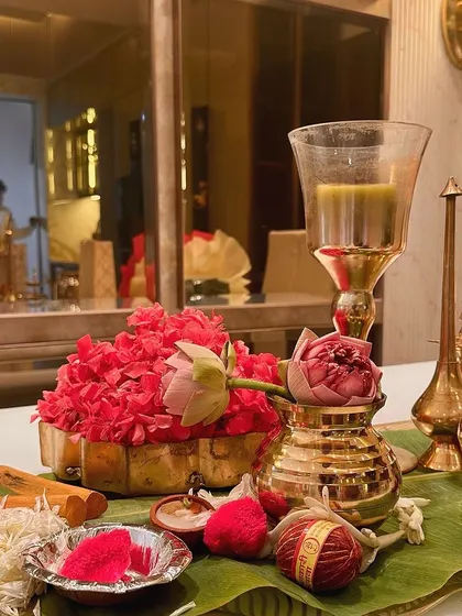 A table setting for a housewarming, with traditional brass items and fresh flowers reflected in a modern mirror. This shows how we blend traditional elements into contemporary homes.