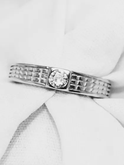 A classic men's band ring featuring a textured grid pattern and a central, bezel-set solitaire stone. This piece balances traditional design with a touch of modern detail.