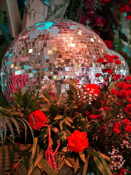 A disco ball nestled amongst red flowers and tropical leaves. This detail shot captures the essence of the 'Jungle Disco' theme, blending glamour with natural elements.