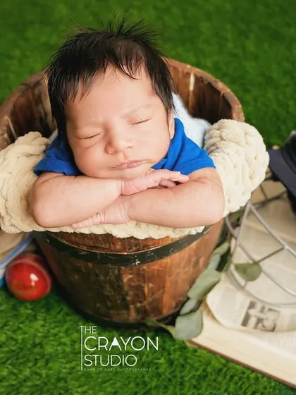 The future cricket star dreams of victory, sleeping in a bucket surrounded by all the essential gear: helmet, gloves, and trophy.